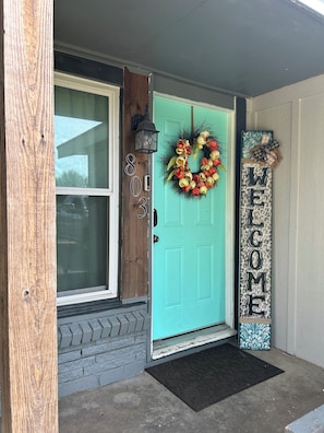 Une porte d’entrée turquoise ornée d’une guirlande de fleurs, d’une pancarte de bienvenue et d’une boîte aux lettres.