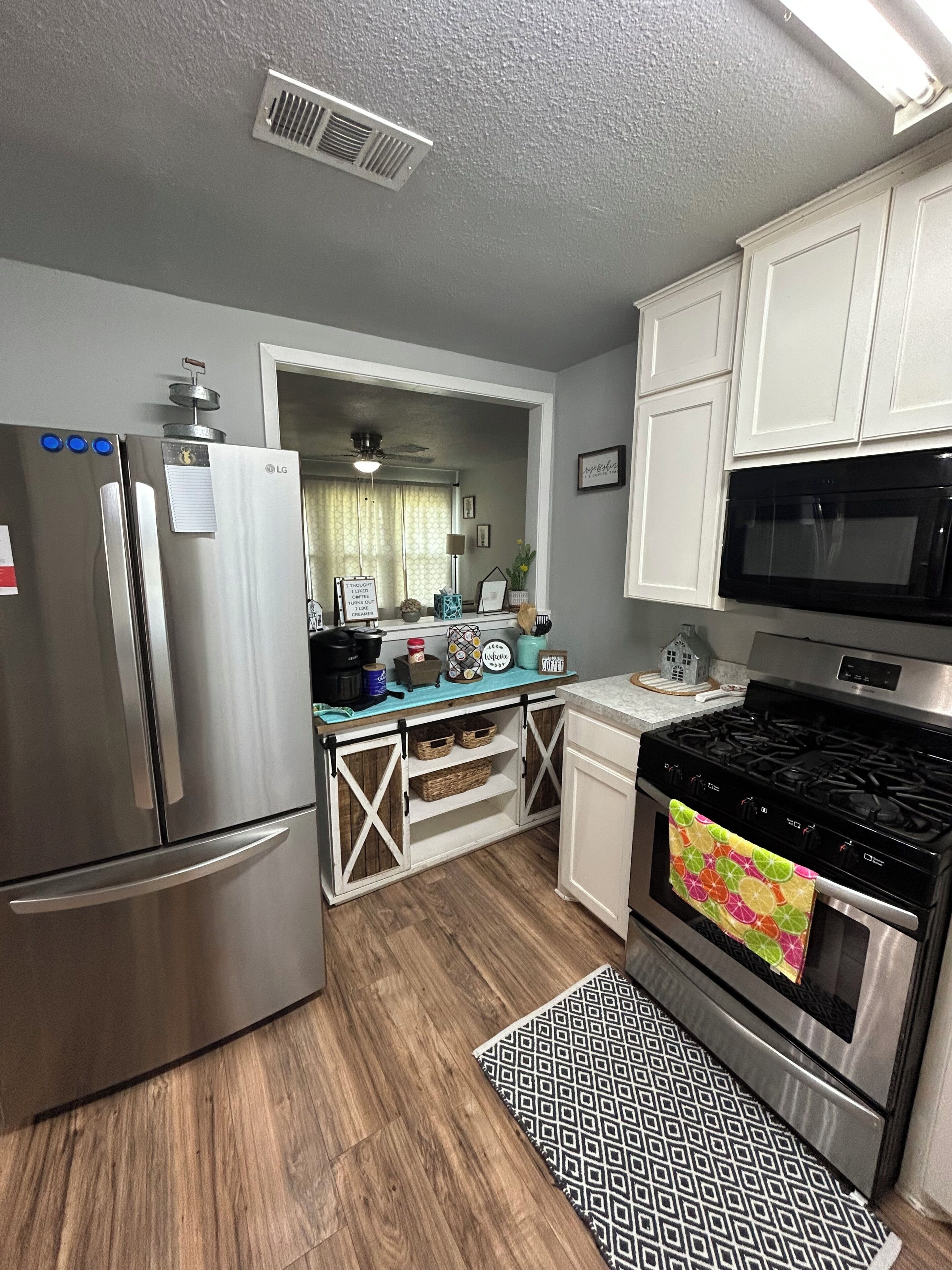 A compact kitchen with a refrigerator, stove, microwave, and a window with curtains.
