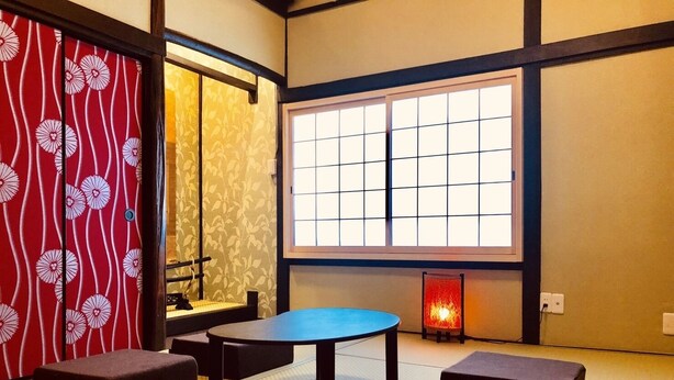 A tatami mat room with a low table and cushions, a shoji screen, and a window with a grid pattern.