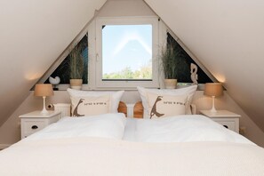 A bedroom with a sloped ceiling, a large window, two bedside tables with lamps, and two decorative pillows with coordinates. - Erika - House Erika, Germany (Sylt)