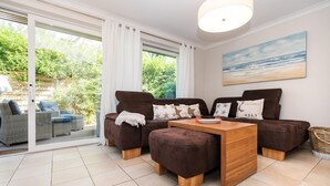A cozy living area with a sofa set, a wooden coffee table, and a view of greenery through large windows. - Erika - House Erika, Germany (Sylt)