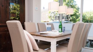 A dining area with a wooden table, beige upholstered chairs, and a green bottle on the table. - Erika - House Erika, Germany (Sylt)