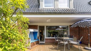 A patio area with a table and chairs, a striped beach chair, and a covered seating area. - Driftwood - House Driftwood (Sylt)