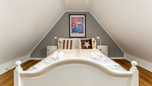 A bedroom with a sloped ceiling, a bed with white bedding, two bedside tables with lamps, and a framed picture on the wall. - Driftwood - House Driftwood (Sylt)