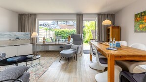 A modern living room with a dining area, large windows, and a view of the garden. - Driftwood - House Driftwood (Sylt)