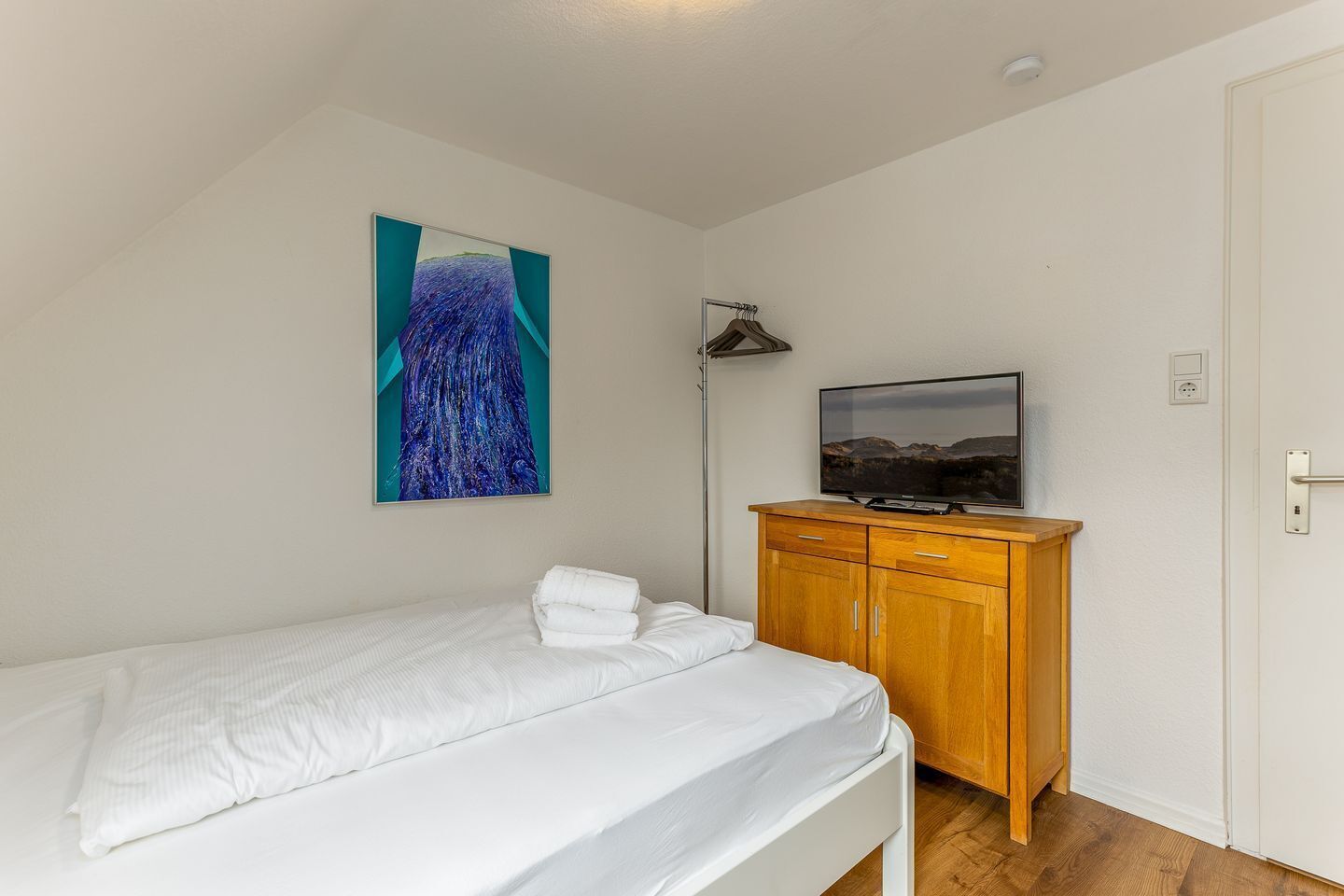 Quarto com cama, cómoda de madeira, televisão e um quadro na parede.