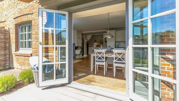 Une maison moderne dotée d’un vaste patio, d’un coin repas et d’une cuisine visible à travers de grandes portes vitrées.
