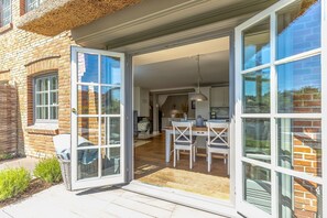 A modern house with a spacious patio, a dining area, and a kitchen visible through large glass doors. - Herzzeit - HeartTime, Germany (Sylt)