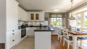 Une cuisine moderne avec des meubles blancs, un îlot central et un coin repas comprenant des chaises blanches et une table en bois.