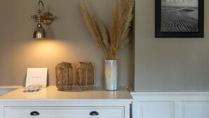 Une commode blanche ornée d’un tableau encadré, une lampe fixée au mur et un vase contenant des plumes d’herbe des pampas.