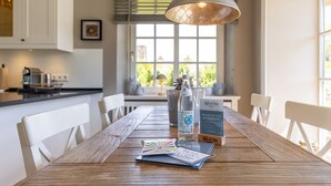 Une table à manger en bois, entourée de chaises, avec une bouteille d’eau, un menu et un panneau d’affichage, le tout dans une pièce lumineuse dotée d’une fenêtre et d’un luminaire suspendu.