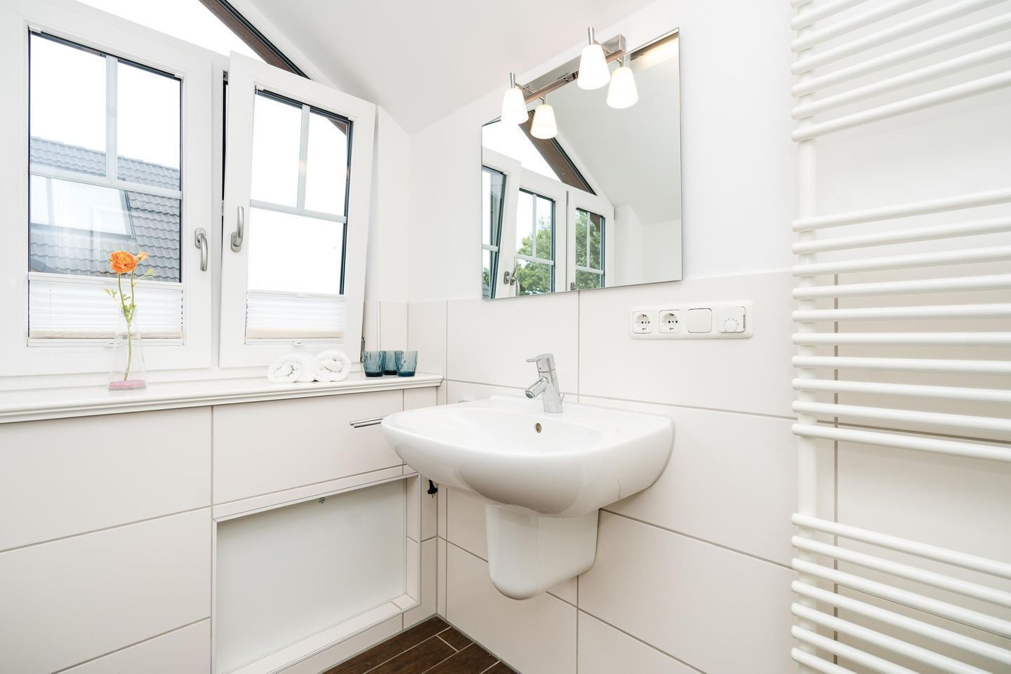 Ein modernes Badezimmer mit einem weißen Waschbecken, großen Fenstern und einem Handtuchhalter.