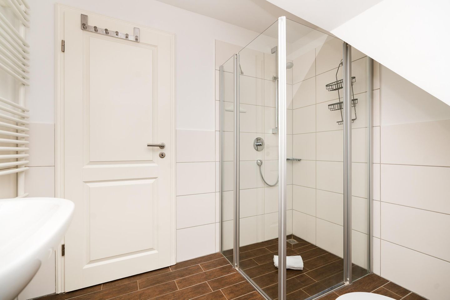 Une salle de bain moderne avec une douche à parois de verre, une porte blanche et un sol carrelé de couleur marron.