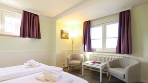 A hotel room with two beds, a chair, a table, and a radiator. - Rochts - House Rolf - Apartment Rochts (Sylt)