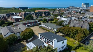 An aerial view of a residential area with houses, a parking lot, and a view of the sea. - Rochts - House Rolf - Apartment Rochts (Sylt)