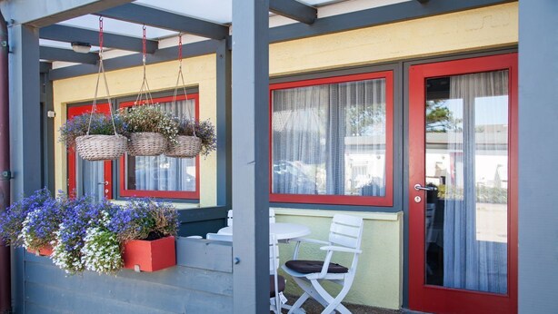 A covered porch with a red door, white chairs, and hanging baskets with flowers. - Rochts - House Rolf - Apartment Rochts (Sylt)