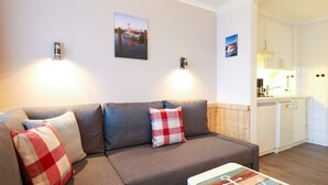 A modern living room with a grey sectional sofa, a small coffee table, and a kitchen area visible through an open doorway. - Rochts - House Rolf - Apartment Rochts (Sylt)