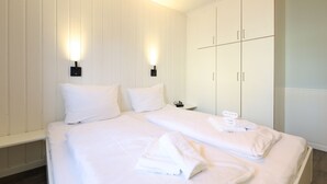 A hotel room with a large bed, two bedside tables, and a wardrobe with two doors. - Left - House Rolf - Left (Sylt)