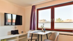 Une chambre d’hôtel équipée d’une télévision, d’une table avec des chaises, d’une fenêtre avec des rideaux et d’un radiateur.