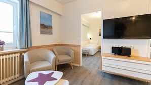 A modern hotel room with a large TV, comfortable seating, a view of the beach, and a cozy atmosphere.