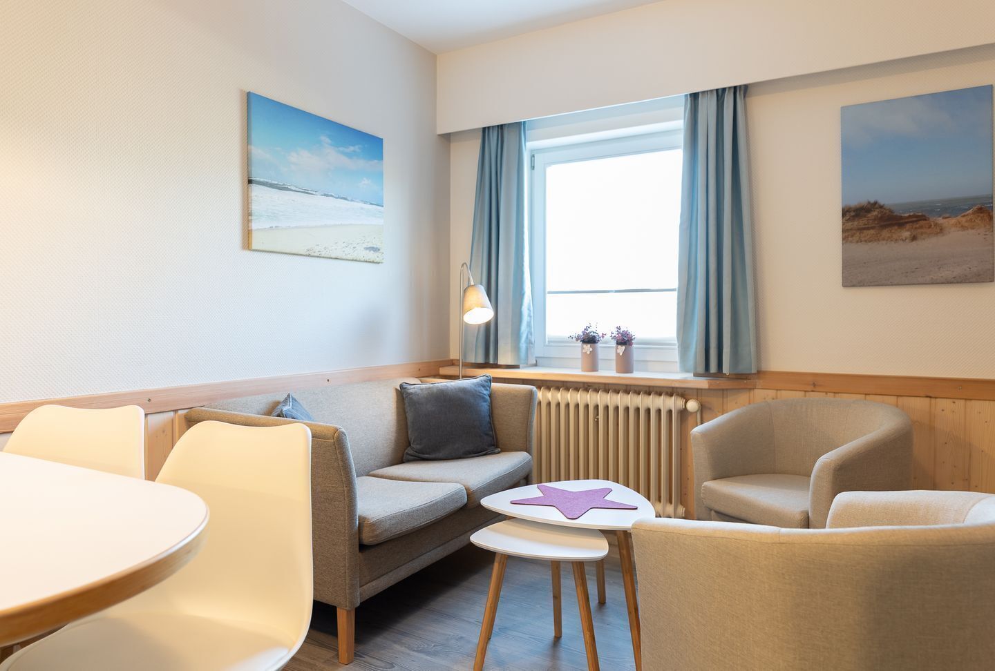 A hotel room with a sofa, two armchairs, a small table, and a window with curtains.
