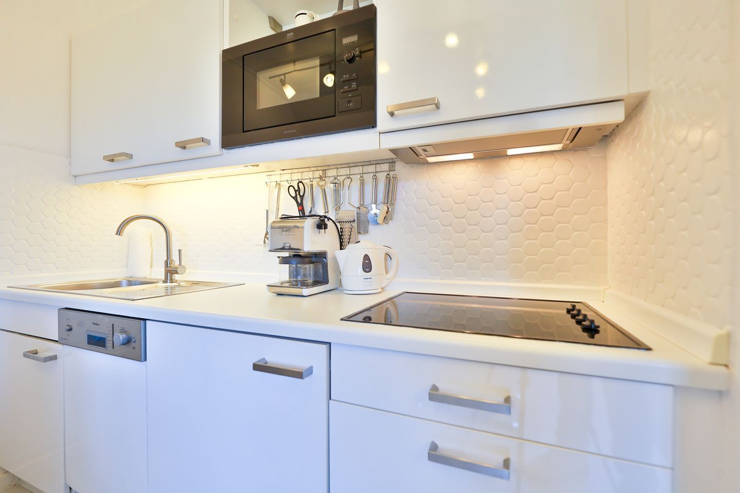 Une cuisine moderne avec des meubles blancs, un four à micro-ondes encastré, une machine à café et une cuisinière à gaz.