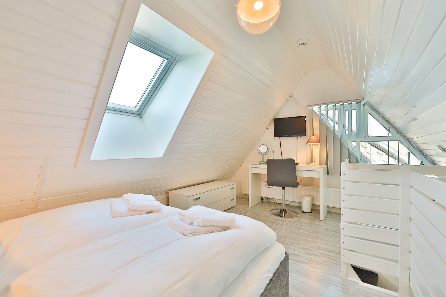 Un dormitorio con tragaluz, un escritorio con silla y una escalera.