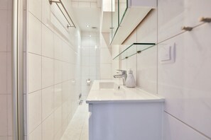 Un baño moderno con azulejos blancos, un lavamanos grande y puertas de ducha de vidrio.