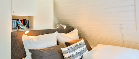 Une chambre confortable avec un lit, des oreillers, une table de chevet et une bibliothèque.