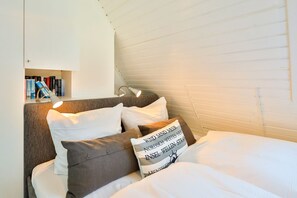 A cozy bedroom with a bed, pillows, a bedside table, and a bookshelf. - Appartement Auszeit, Deutschland (Wenningstedt-Braderup (Sylt))
