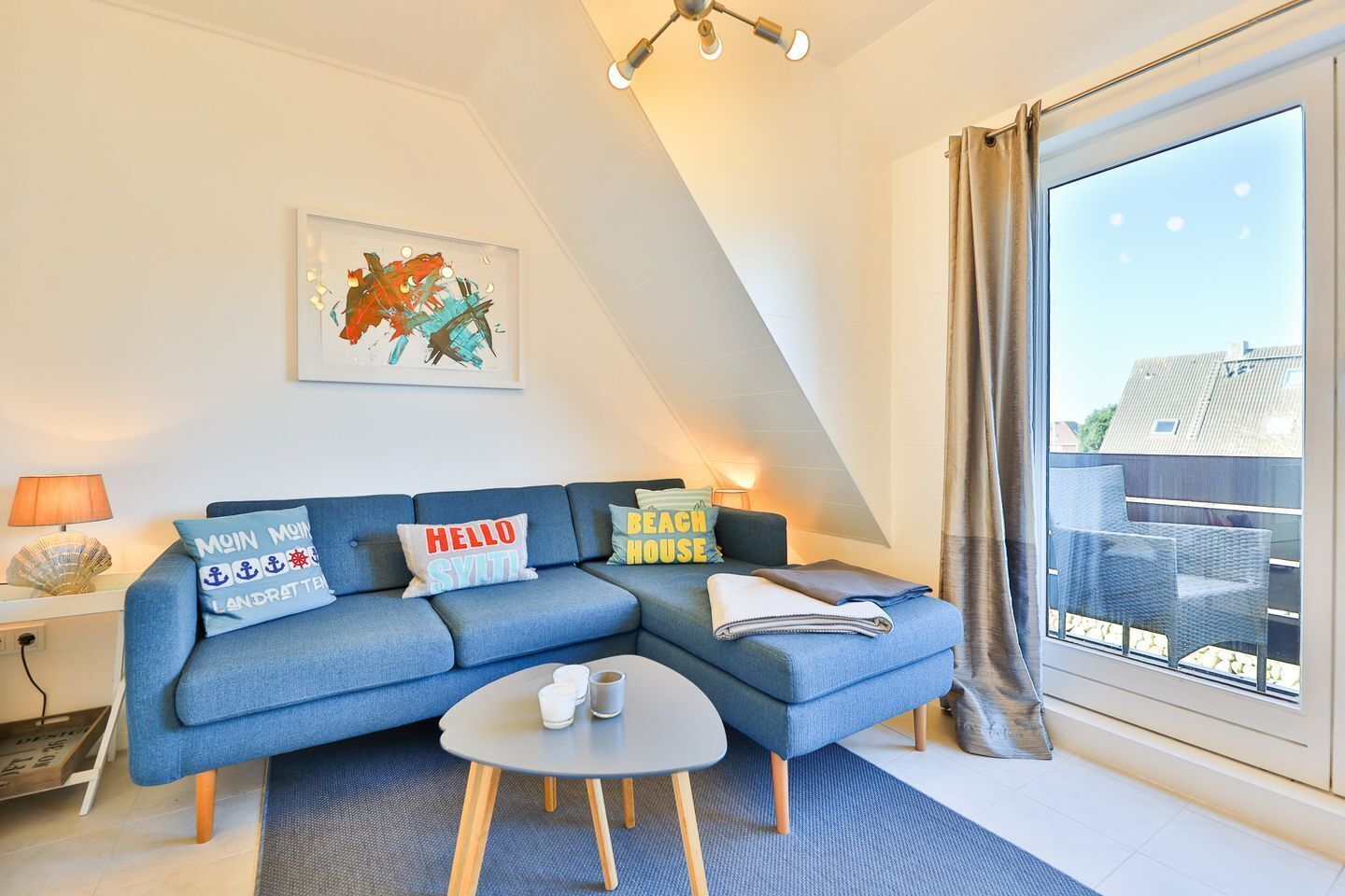 Ein modernes Wohnzimmer mit einem blauen Sofa, einem Couchtisch und einem großen Fenster mit Blick auf Gebäude.
