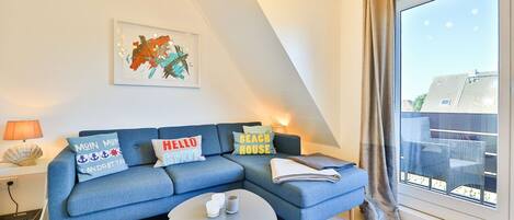Ein modernes Wohnzimmer mit einem blauen Sofa, einem Couchtisch und einem großen Fenster mit Blick auf Gebäude.