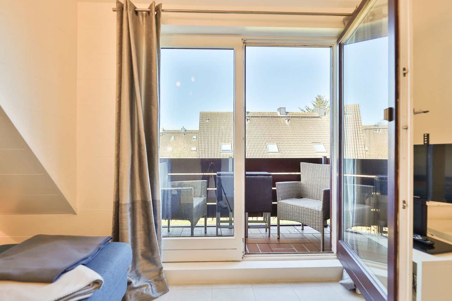 Una stanza con un letto, una finestra con tende, un balcone con tavolo e sedie e una TV.