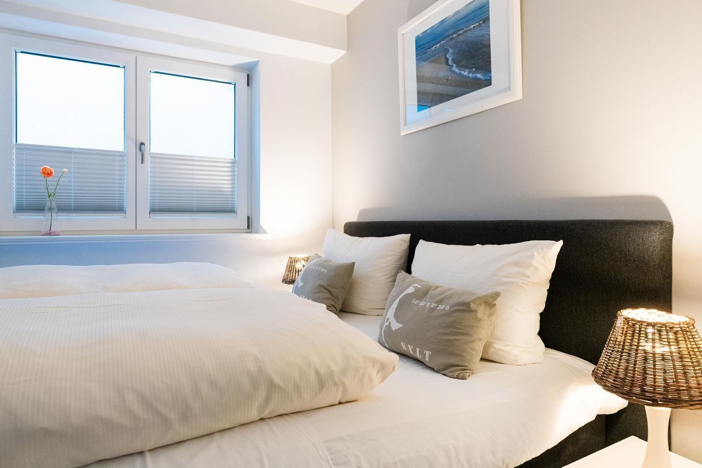 A bedroom with a large bed, a nightstand with a lamp, and a window with blinds.