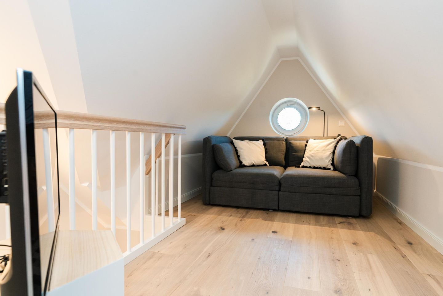 A cozy attic room with a wooden staircase, a grey sofa with cushions, and a skylight.