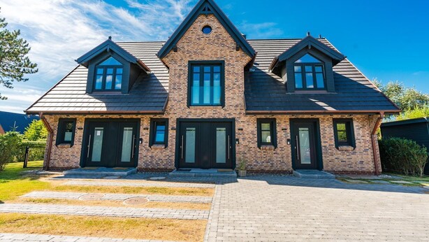 Une maison à deux étages, construite en briques, avec un toit à pignon, de nombreuses fenêtres et une entrée à l’avant.