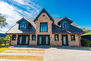 Une maison à deux étages, construite en briques, avec un toit à pignon, de nombreuses fenêtres et une entrée à l’avant.