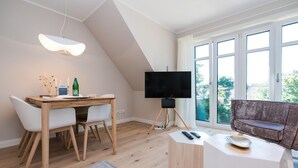 Un salon moderne comprenant un coin repas, un téléviseur posé sur un trépied et une grande fenêtre offrant une belle vue.