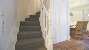 Una escalera con peldaños alfombrados y barandillas blancas que conduce a un cuarto con una puerta blanca y una silla de mimbre.