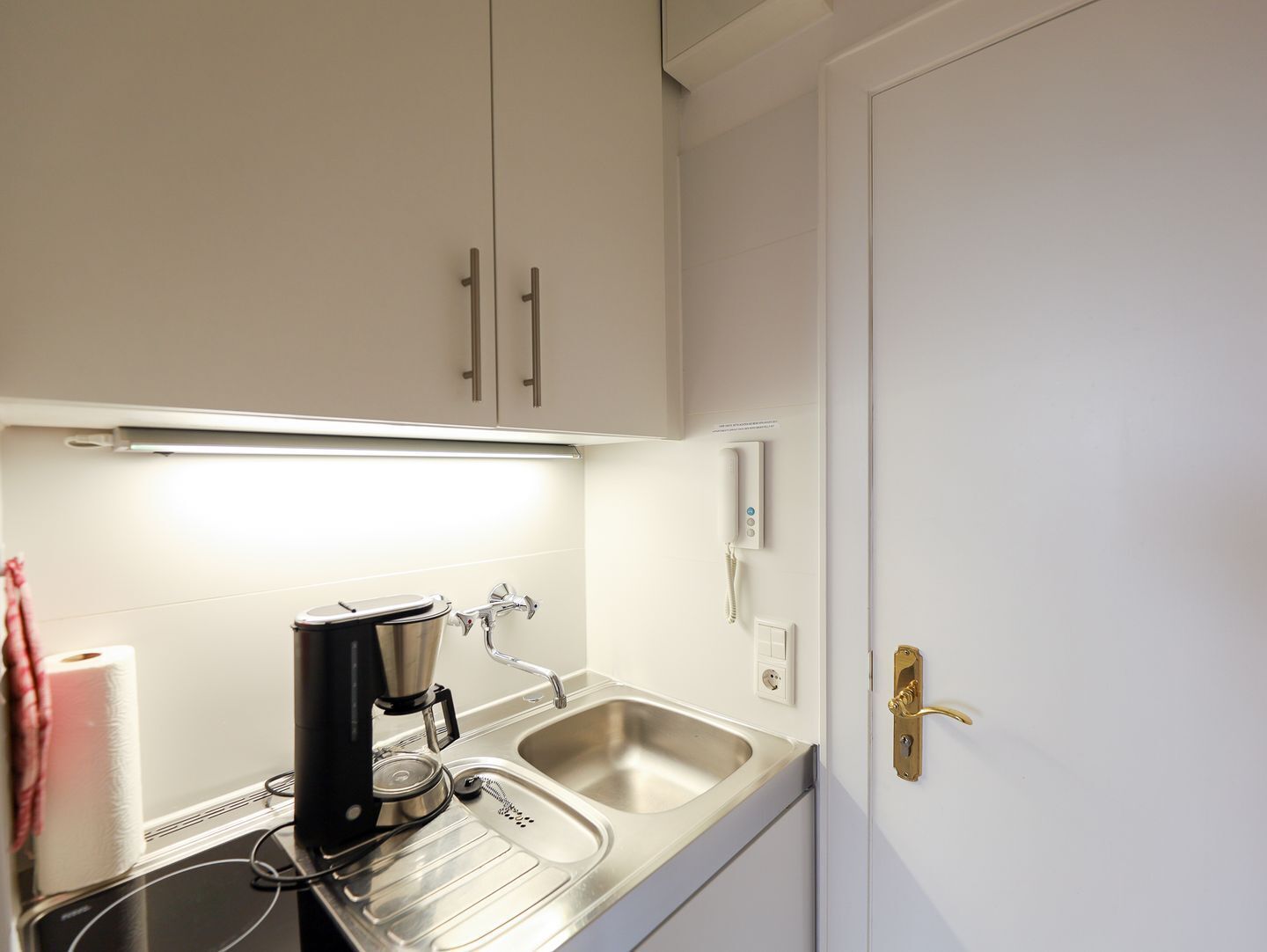 A kitchenette with a coffee maker, a sink, and a door with a brass handle.