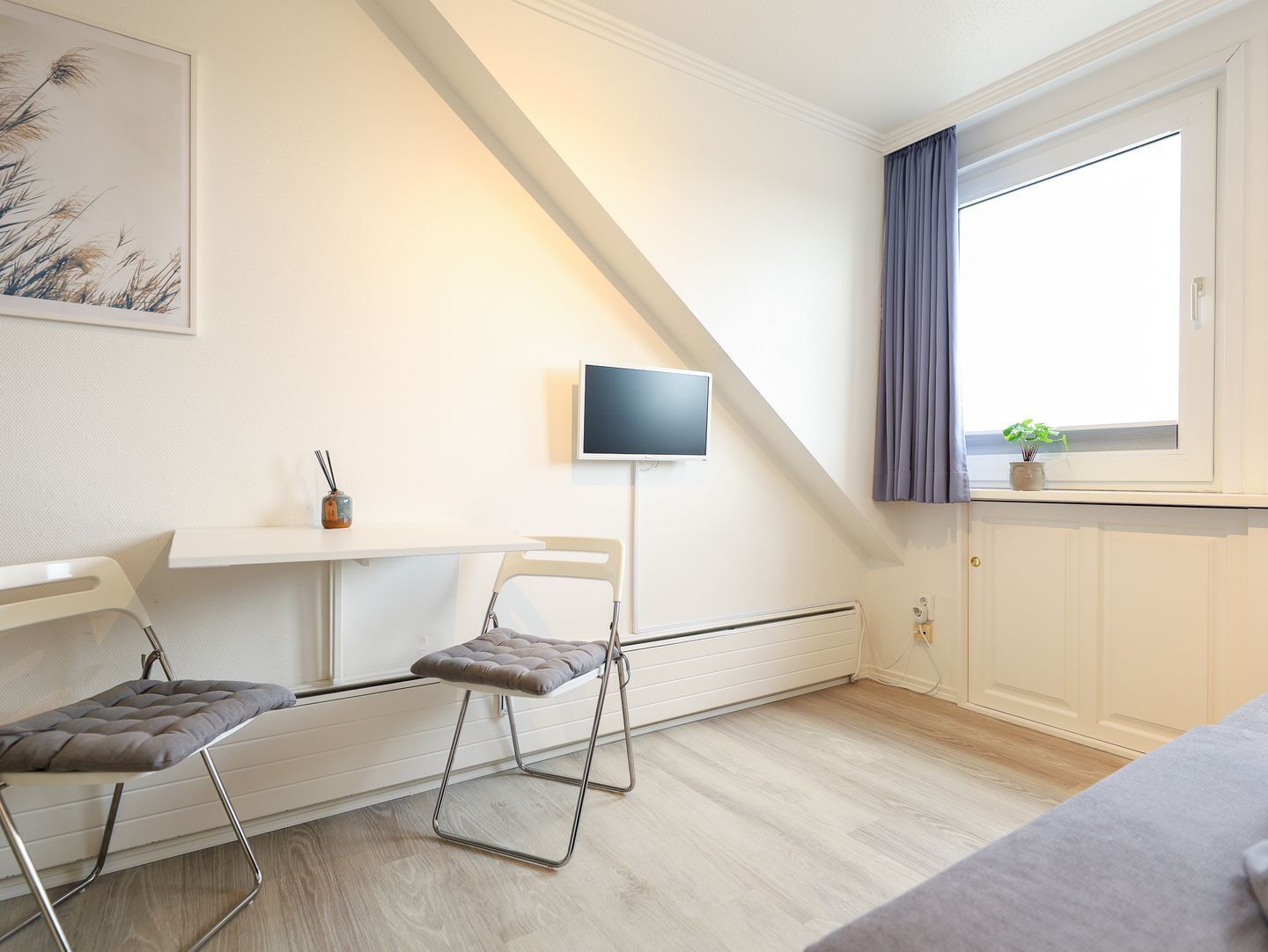 A modern room with a white desk, two chairs, a flat-screen TV, and a window with curtains.
