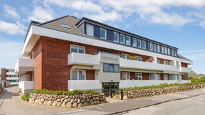 A modern multi-story hotel with a brick facade, white balconies, and a stone wall in front. - Jasper - Hedighuis - Jasper in the Hedighuis (Sylt)