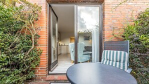 A patio with a table and two chairs, a brick wall, and a sliding glass door leading to an interior space with a sofa and a lamp.