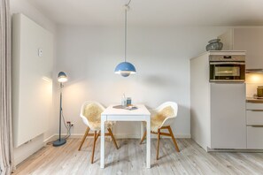 Et moderne køkken med et hvidt køleskab, en indbygget ovn og en blå pendellampe over et hvidt bord med to stole.
