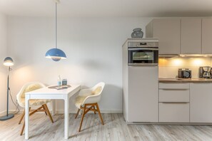 Et moderne køkken med et hvidt bord, to stole, en blå hængende lampe og en indbygget ovn.