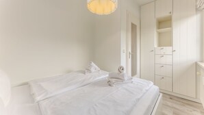 A minimalist bedroom with a bed, a hanging light fixture, and a wardrobe.