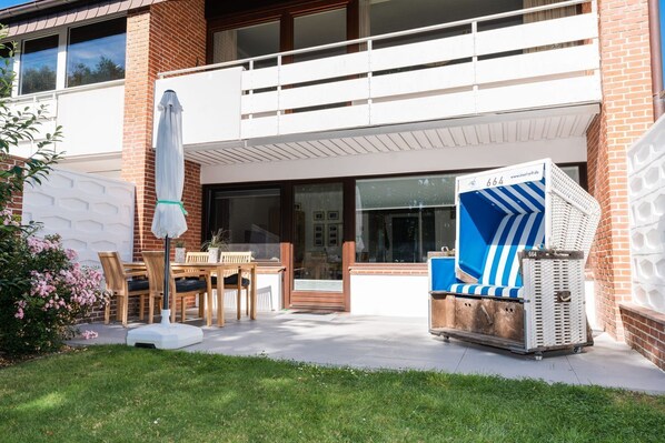 A modern house with a covered patio, a dining area with wooden furniture, and a blue and white striped chair. - Appartement Emhüs, Deutschland (Sylt)