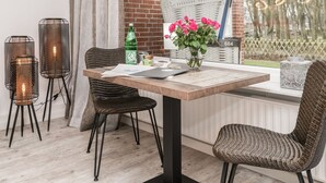 Un coin repas avec une table en bois, des chaises en osier, un vase rempli de fleurs et deux lampes hautes, cylindriques, dotées d’un abat-jour en treillis.
