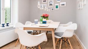 A dining area with a white table, four white chairs, a vase of flowers, and framed pictures on the wall. - Strandhütte - House Strandhütte (Sylt)