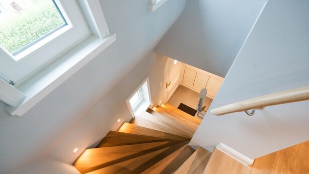 A modern staircase with wooden steps and a handrail, leading to a kitchen area with cabinets and a window. - Strandhütte - House Strandhütte (Sylt)